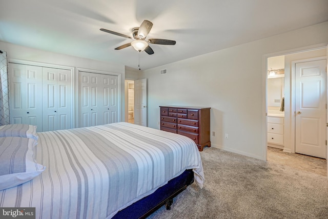 bedroom featuring multiple closets, ensuite bathroom, light colored carpet, and ceiling fan