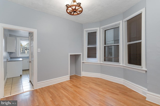 empty room featuring an inviting chandelier, a textured ceiling, and light hardwood / wood-style floors