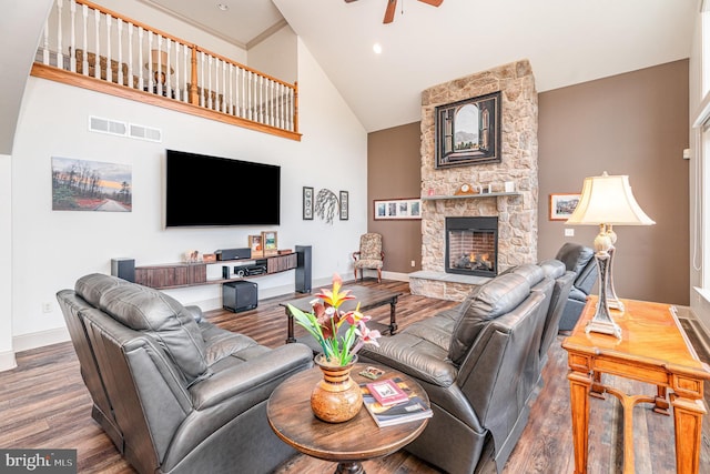 living area with visible vents, high vaulted ceiling, a ceiling fan, wood finished floors, and a stone fireplace