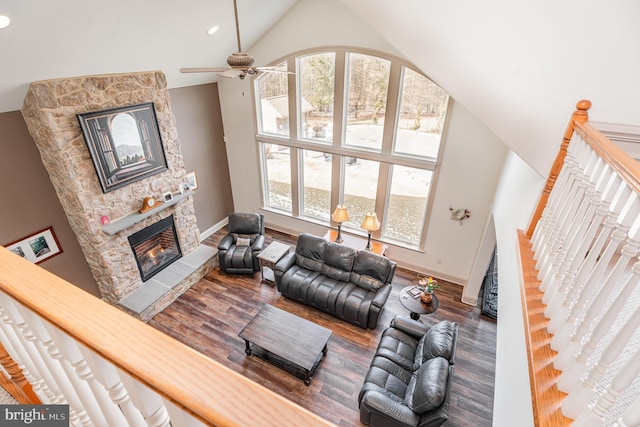 living area with high vaulted ceiling, wood finished floors, a stone fireplace, baseboards, and ceiling fan