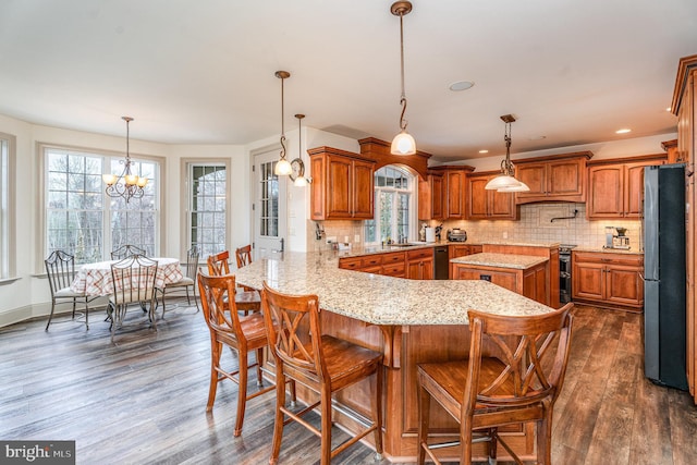 kitchen featuring a chandelier, a peninsula, freestanding refrigerator, brown cabinetry, and dark wood-style flooring