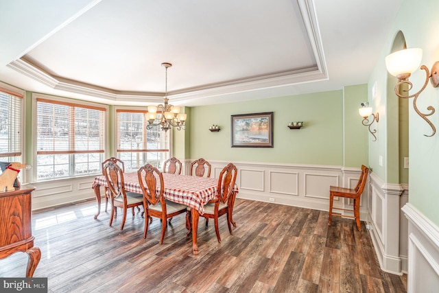 dining space with dark wood-type flooring, a tray ceiling, crown molding, a decorative wall, and a chandelier