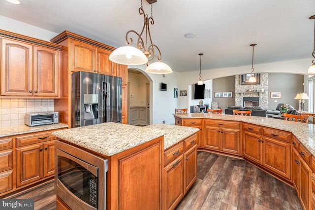 kitchen with backsplash, a kitchen island, stainless steel appliances, a fireplace, and dark wood-style flooring