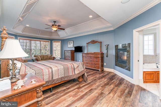 bedroom with crown molding, baseboards, wood finished floors, a glass covered fireplace, and a ceiling fan