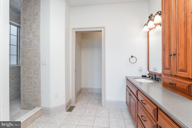 bathroom featuring tile patterned flooring, tiled shower, vanity, and baseboards