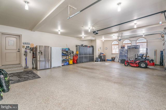 garage with a garage door opener, stainless steel fridge with ice dispenser, and freestanding refrigerator