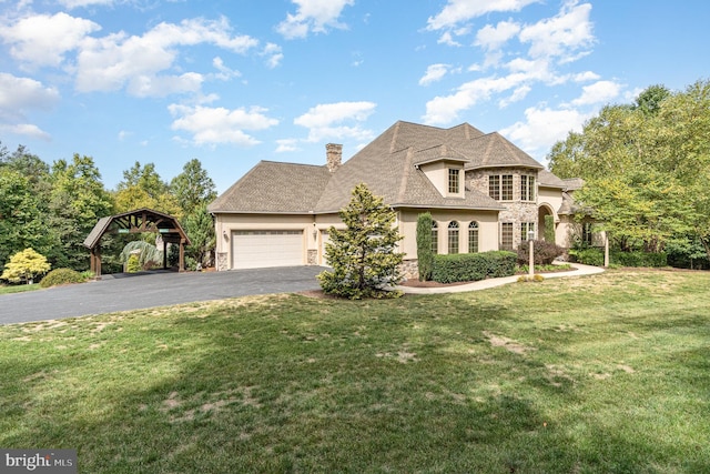 french country home featuring aphalt driveway, stone siding, an attached garage, a front yard, and a chimney