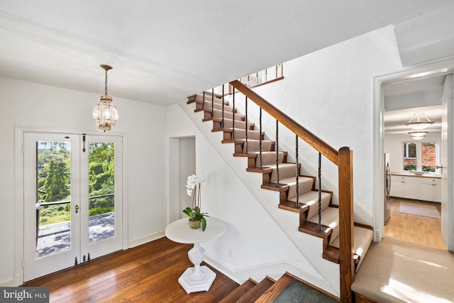 staircase featuring an inviting chandelier, french doors, and hardwood / wood-style floors