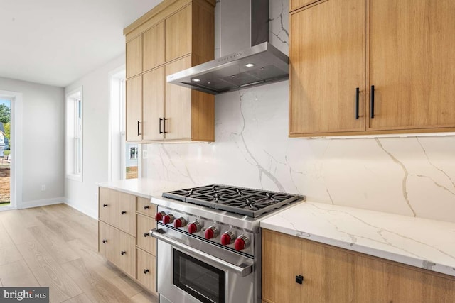 kitchen featuring tasteful backsplash, wall chimney exhaust hood, light stone counters, premium range, and light hardwood / wood-style flooring