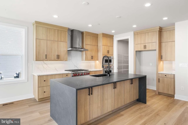 kitchen featuring light hardwood / wood-style floors, wall chimney range hood, sink, and a center island with sink