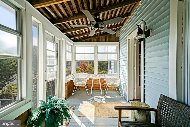 unfurnished sunroom featuring ceiling fan, lofted ceiling with beams, and a wealth of natural light