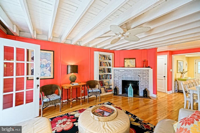 living room featuring hardwood / wood-style flooring, beamed ceiling, ceiling fan, and a brick fireplace