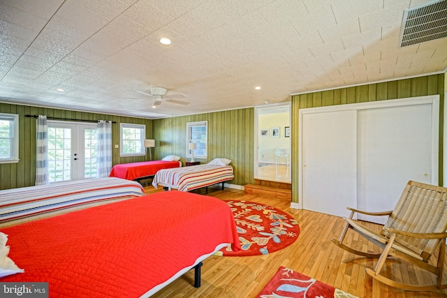 bedroom with wood walls, access to exterior, hardwood / wood-style flooring, and ceiling fan