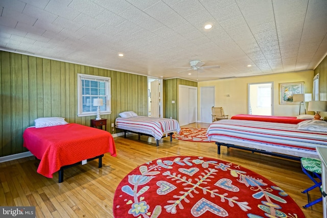 bedroom with hardwood / wood-style flooring, wooden walls, and ceiling fan