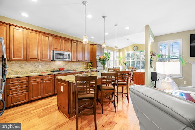 kitchen featuring stainless steel appliances, a healthy amount of sunlight, a center island with sink, and decorative light fixtures