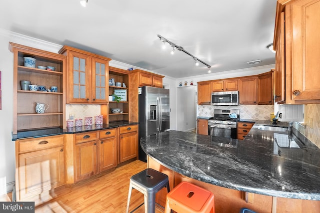 kitchen featuring light hardwood / wood-style flooring, stainless steel appliances, dark stone counters, crown molding, and a breakfast bar