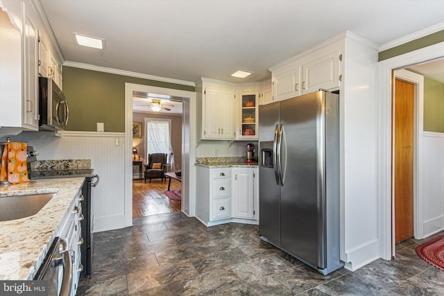 kitchen with ceiling fan, appliances with stainless steel finishes, white cabinetry, ornamental molding, and light stone counters