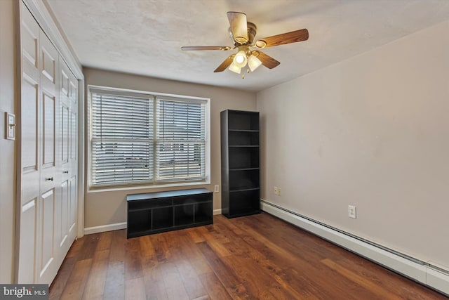 unfurnished bedroom featuring a closet, a baseboard heating unit, ceiling fan, and dark hardwood / wood-style floors