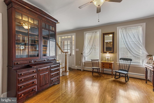 living area featuring ornamental molding, baseboard heating, light wood-type flooring, and ceiling fan