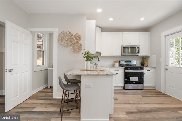 kitchen with light stone countertops, white cabinets, stainless steel appliances, and light wood-type flooring