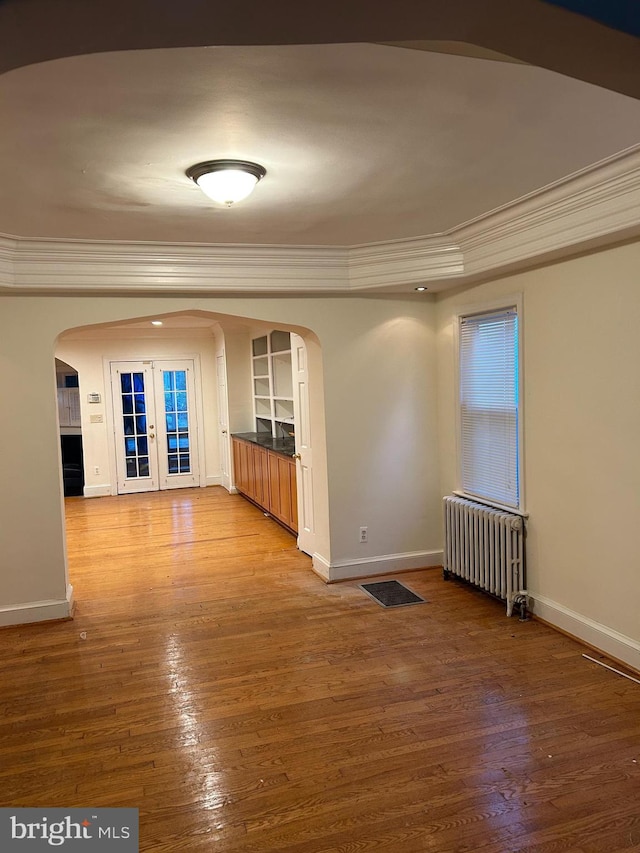 empty room featuring radiator heating unit, baseboards, arched walkways, and ornamental molding