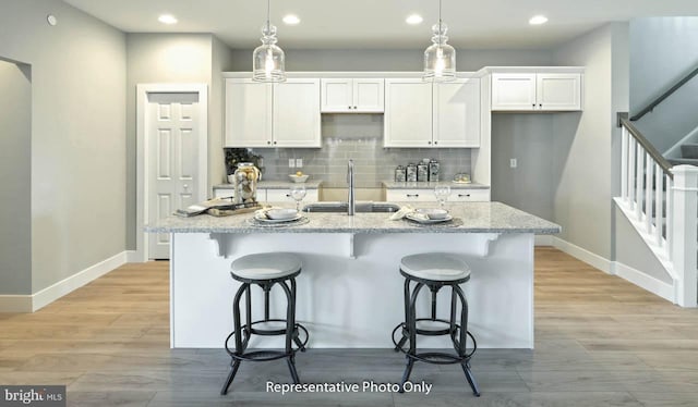 kitchen featuring white cabinets, sink, light stone counters, and an island with sink