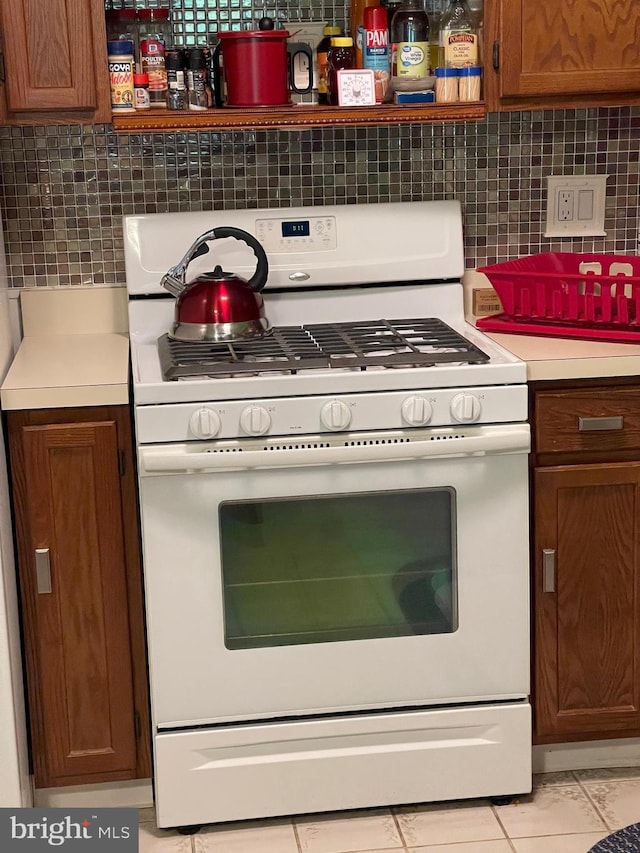 kitchen featuring white range with gas stovetop, decorative backsplash, and light tile patterned floors