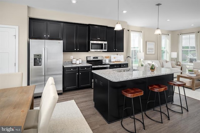 kitchen with an island with sink, hanging light fixtures, stainless steel appliances, a breakfast bar, and dark hardwood / wood-style flooring