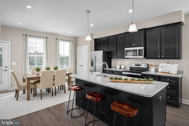 kitchen with a kitchen island with sink, appliances with stainless steel finishes, pendant lighting, and dark hardwood / wood-style floors