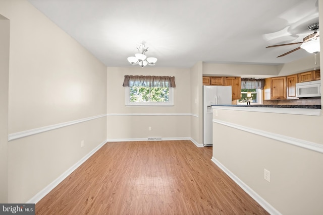 interior space featuring ceiling fan with notable chandelier, light wood-type flooring, white appliances, and plenty of natural light