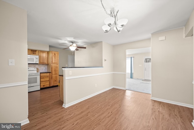 kitchen featuring white appliances, wood-type flooring, decorative light fixtures, ceiling fan with notable chandelier, and tasteful backsplash