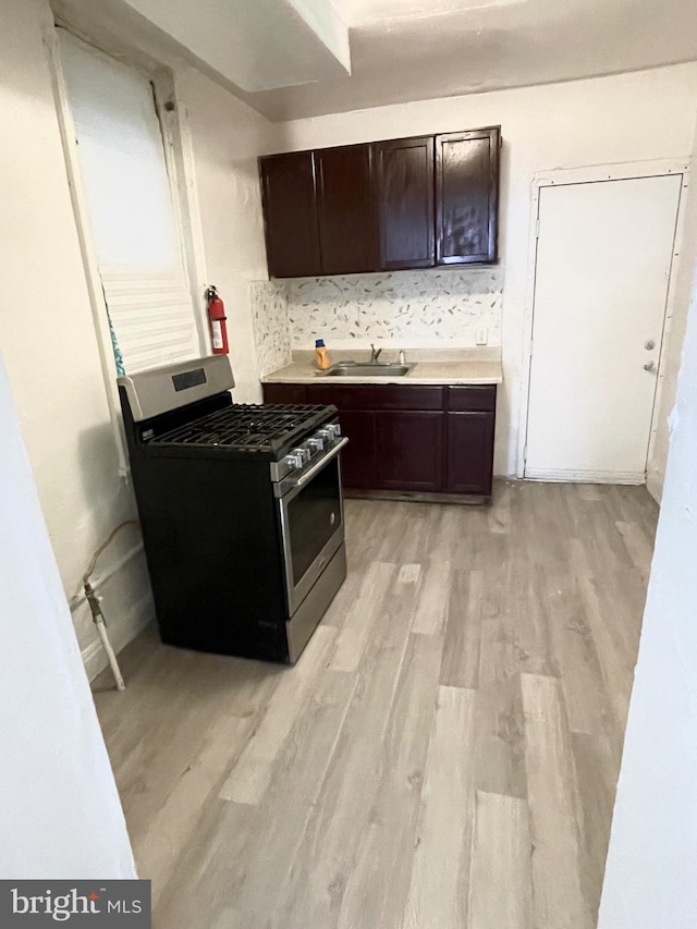 kitchen featuring sink, dark brown cabinets, light hardwood / wood-style floors, and gas range