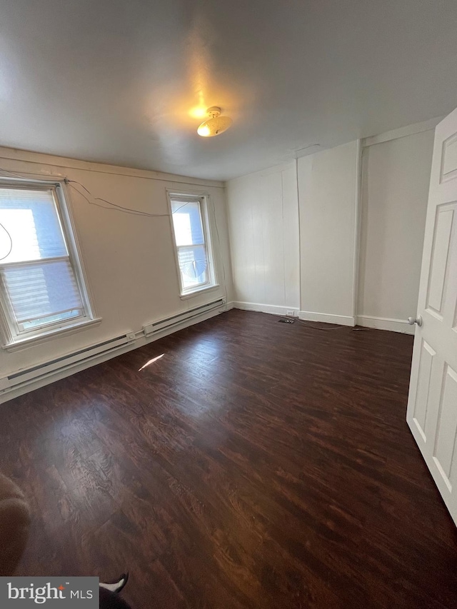 spare room with a baseboard radiator, dark wood-type flooring, and a healthy amount of sunlight