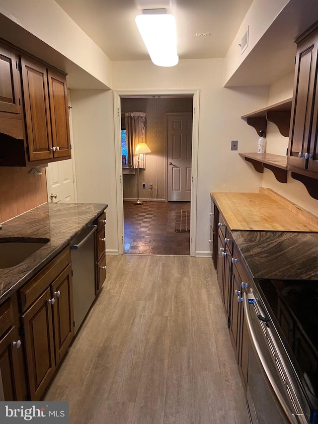 kitchen with appliances with stainless steel finishes, dark brown cabinets, light hardwood / wood-style floors, and wood counters