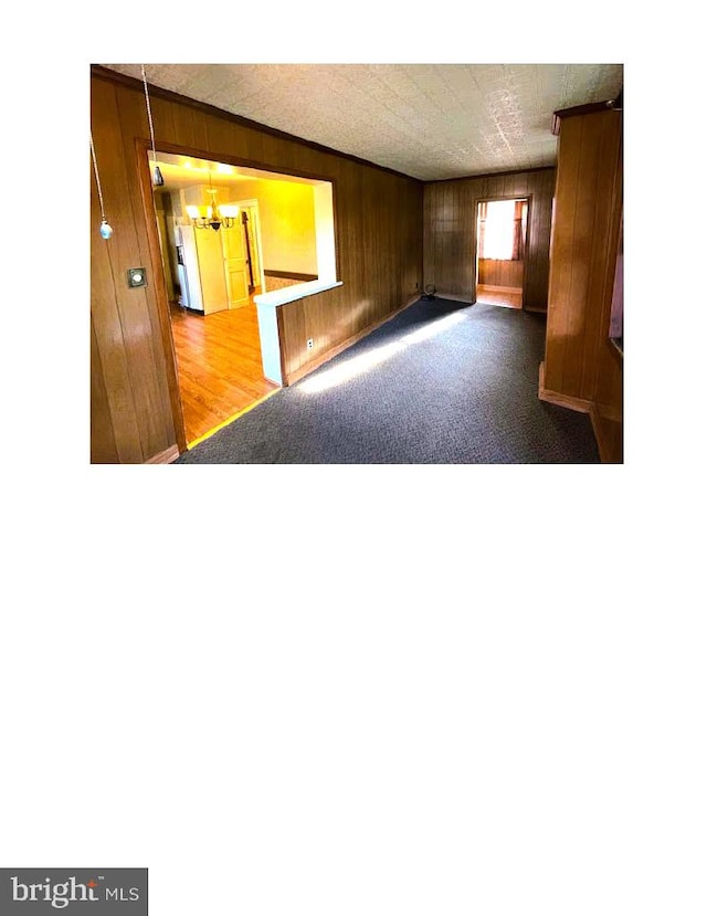 spare room featuring wood-type flooring, wooden walls, and a chandelier