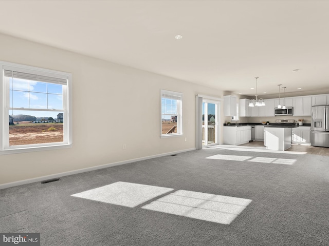 unfurnished living room with a notable chandelier, a wealth of natural light, and light colored carpet