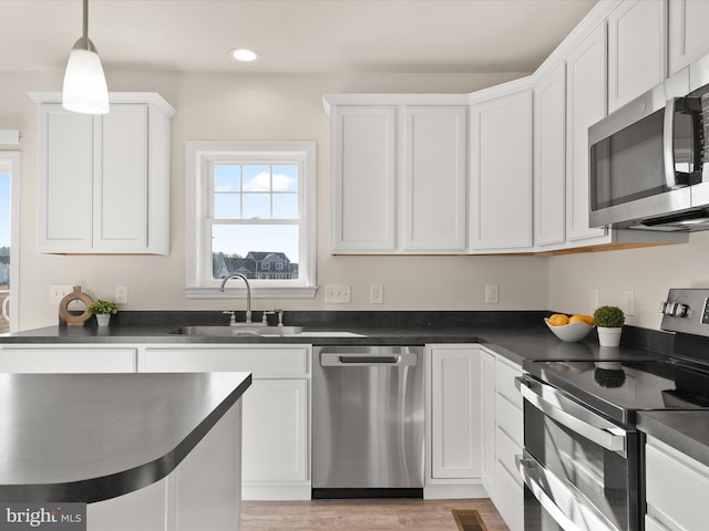 kitchen featuring hanging light fixtures, sink, white cabinets, light wood-type flooring, and appliances with stainless steel finishes