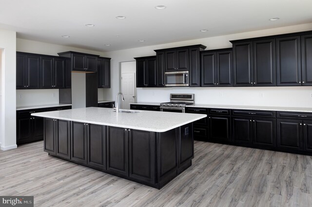 kitchen featuring an island with sink, stainless steel appliances, sink, light stone counters, and light hardwood / wood-style floors