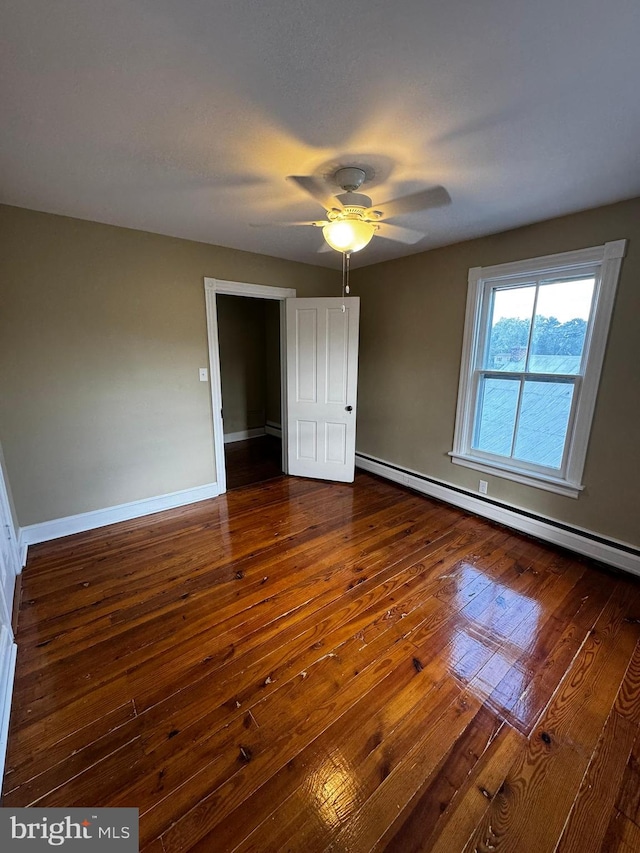 unfurnished bedroom with ceiling fan, baseboard heating, and dark hardwood / wood-style floors