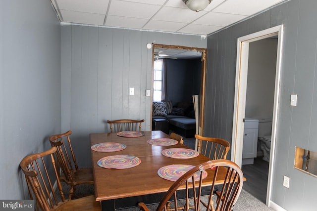 dining room featuring a drop ceiling and wooden walls