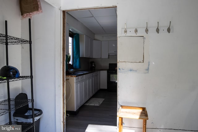 kitchen featuring a drop ceiling, black stove, white cabinets, and dark wood-type flooring