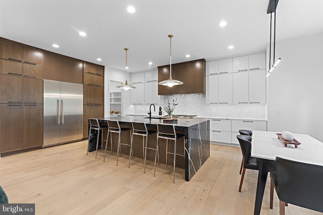 kitchen featuring light hardwood / wood-style floors, hanging light fixtures, a center island with sink, and built in refrigerator