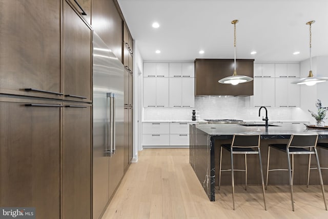 kitchen with white cabinetry, light hardwood / wood-style flooring, pendant lighting, and an island with sink