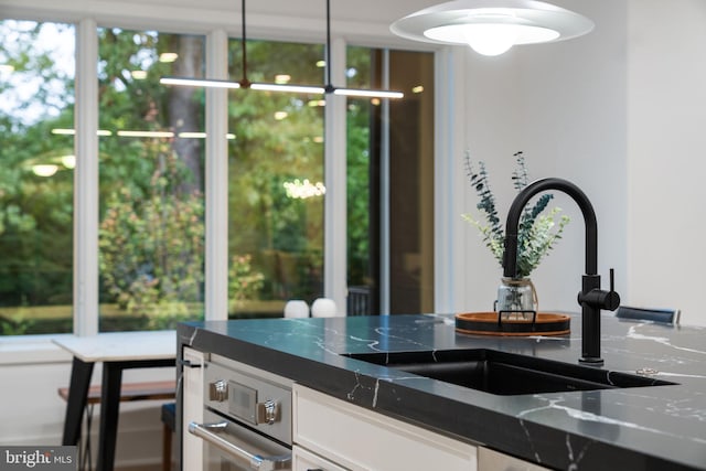 interior space with white cabinetry, decorative light fixtures, dark stone counters, and sink