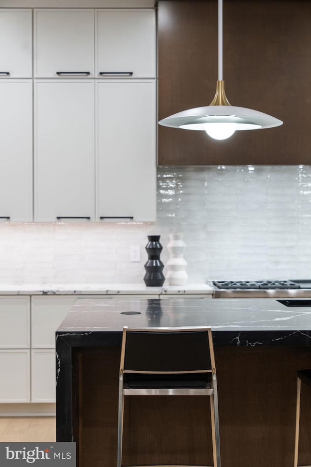 kitchen featuring ventilation hood, white cabinets, hanging light fixtures, and backsplash