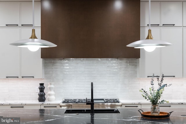 kitchen featuring sink, decorative light fixtures, dark stone countertops, and tasteful backsplash