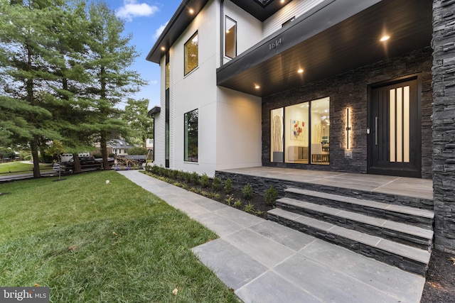 view of exterior entry featuring a patio and a lawn