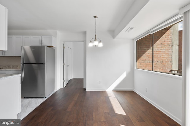 kitchen with wood-type flooring, decorative light fixtures, white cabinets, stainless steel refrigerator, and an inviting chandelier