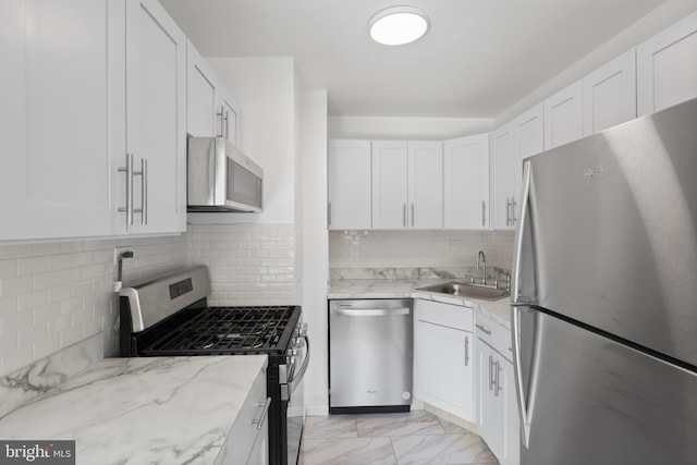 kitchen featuring light stone countertops, appliances with stainless steel finishes, sink, backsplash, and white cabinets