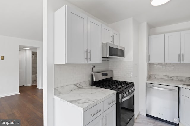 kitchen featuring white cabinets, tasteful backsplash, appliances with stainless steel finishes, light stone countertops, and dark hardwood / wood-style floors